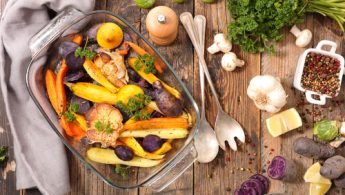 roasted vegetables in a tray on a table with cutlery, vegetables and spices