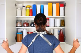 Woman seen from behind opening a food cupboard.
