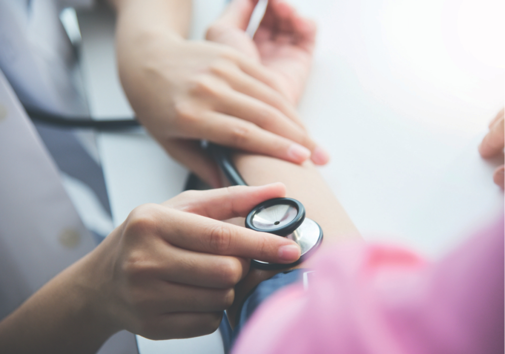 This picture shows a close-up of a healthcare professional using a stethoscope to measure a patient's blood pressure. The focus is on the hands, with one hand holding the stethoscope's diaphragm against the patient's arm while the other hand supports the process.